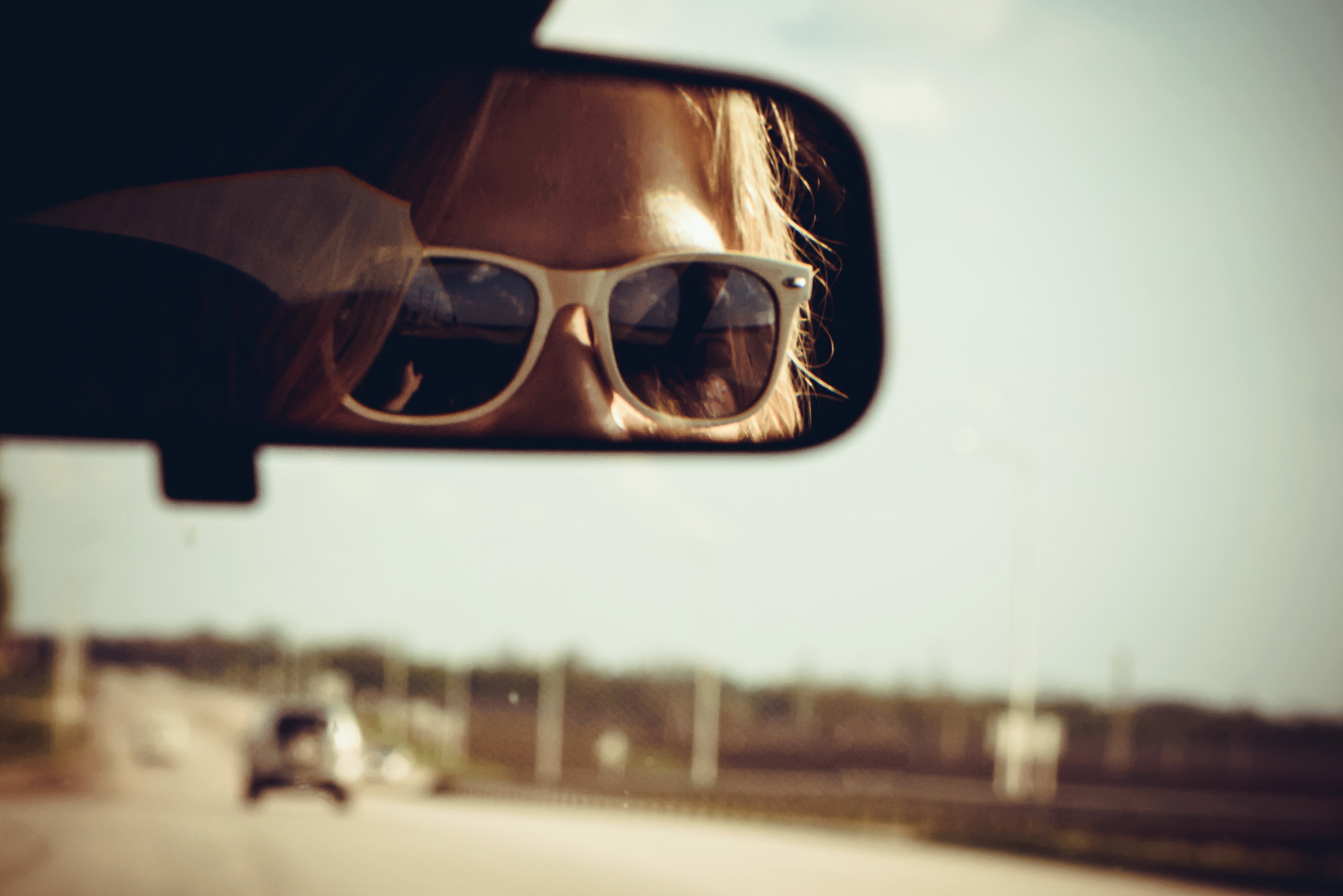 Closeup photo of women the mirror of the car and looking down the road in sunglasses