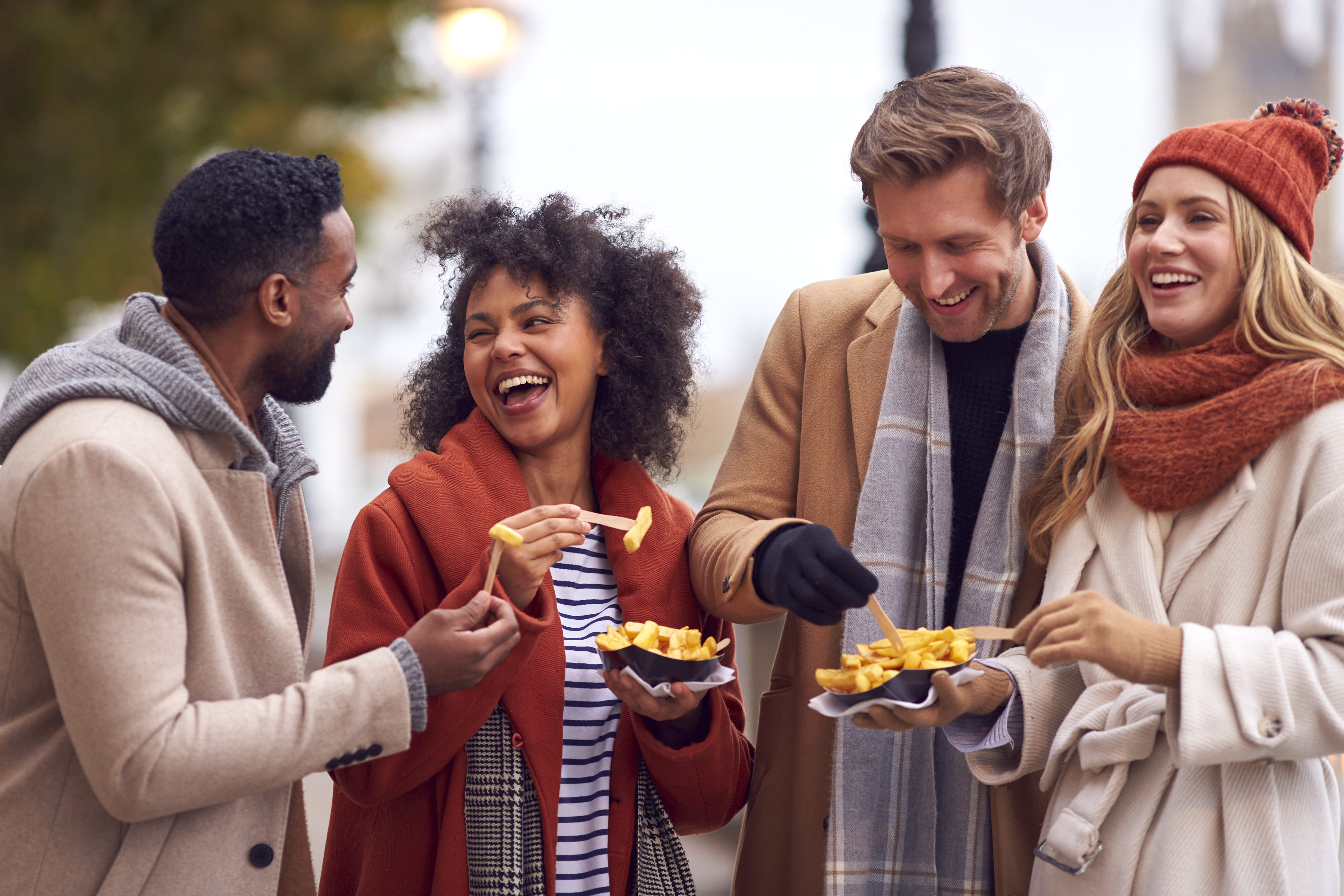 Group Of Friends Outdoors Wearing Coats And Scarves Eating Takeaway Fries In Autumn London